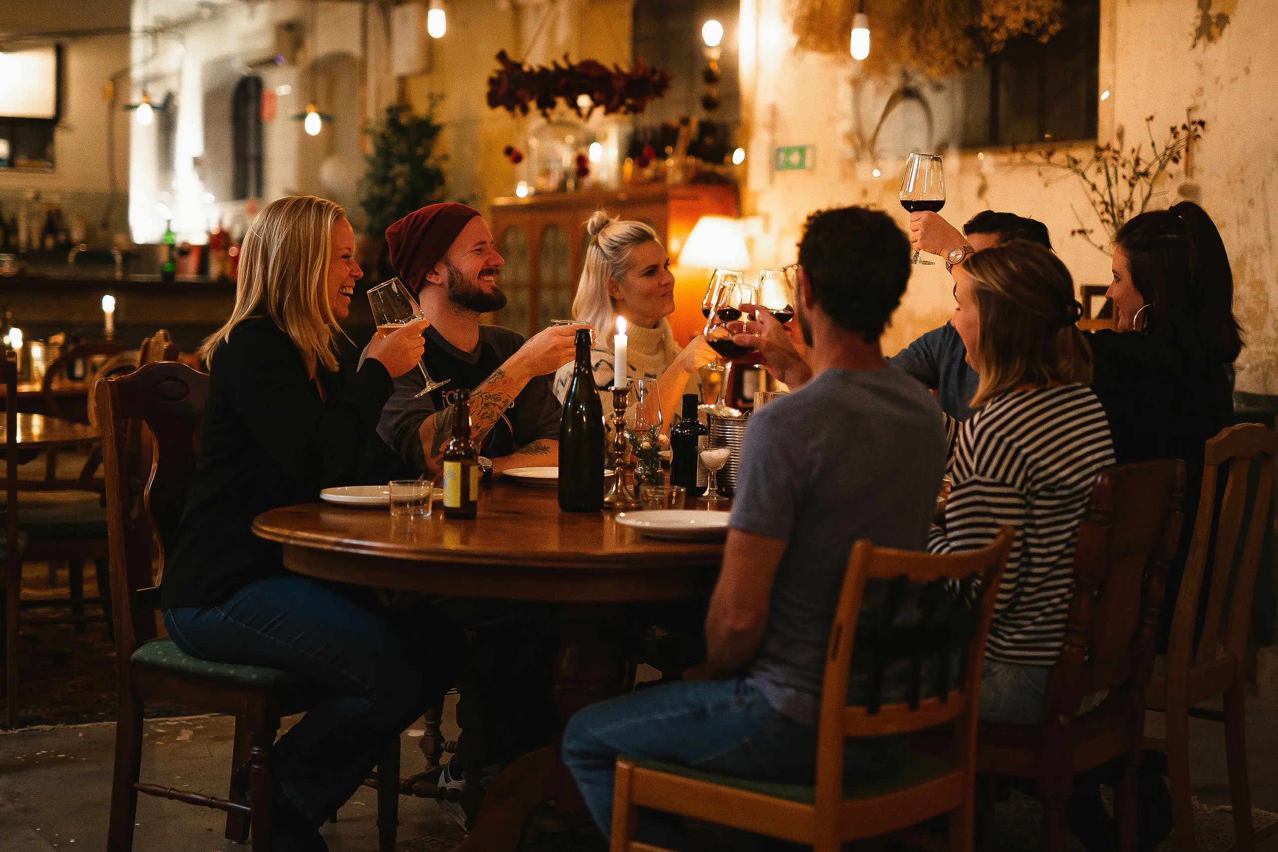 Sällskap som höjer sina glas i en skål i en mörk restaurangmiljö.
