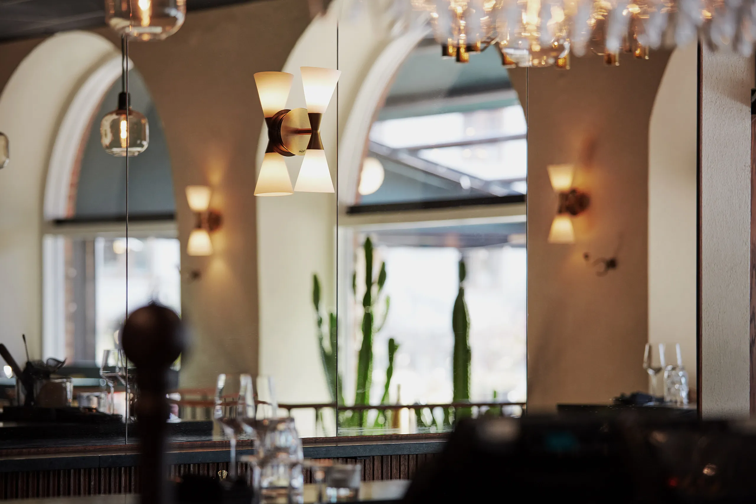 Milgö i retaurnag där välvda fönster syns via en spegelvägg.