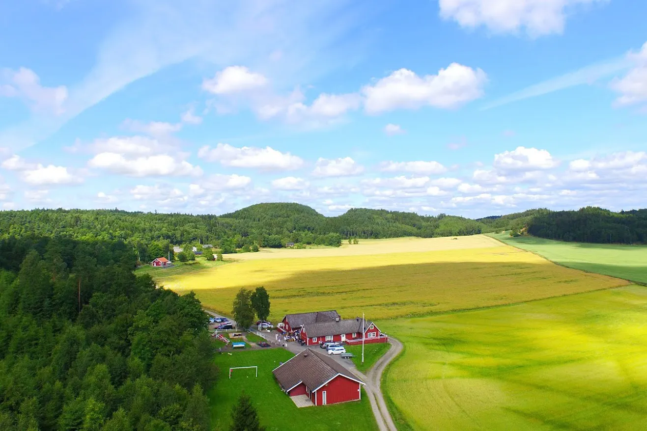 Flygfoto över åkrar, skog och en röd gård.