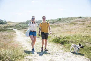 Par med hund som promenerar över strandäng.