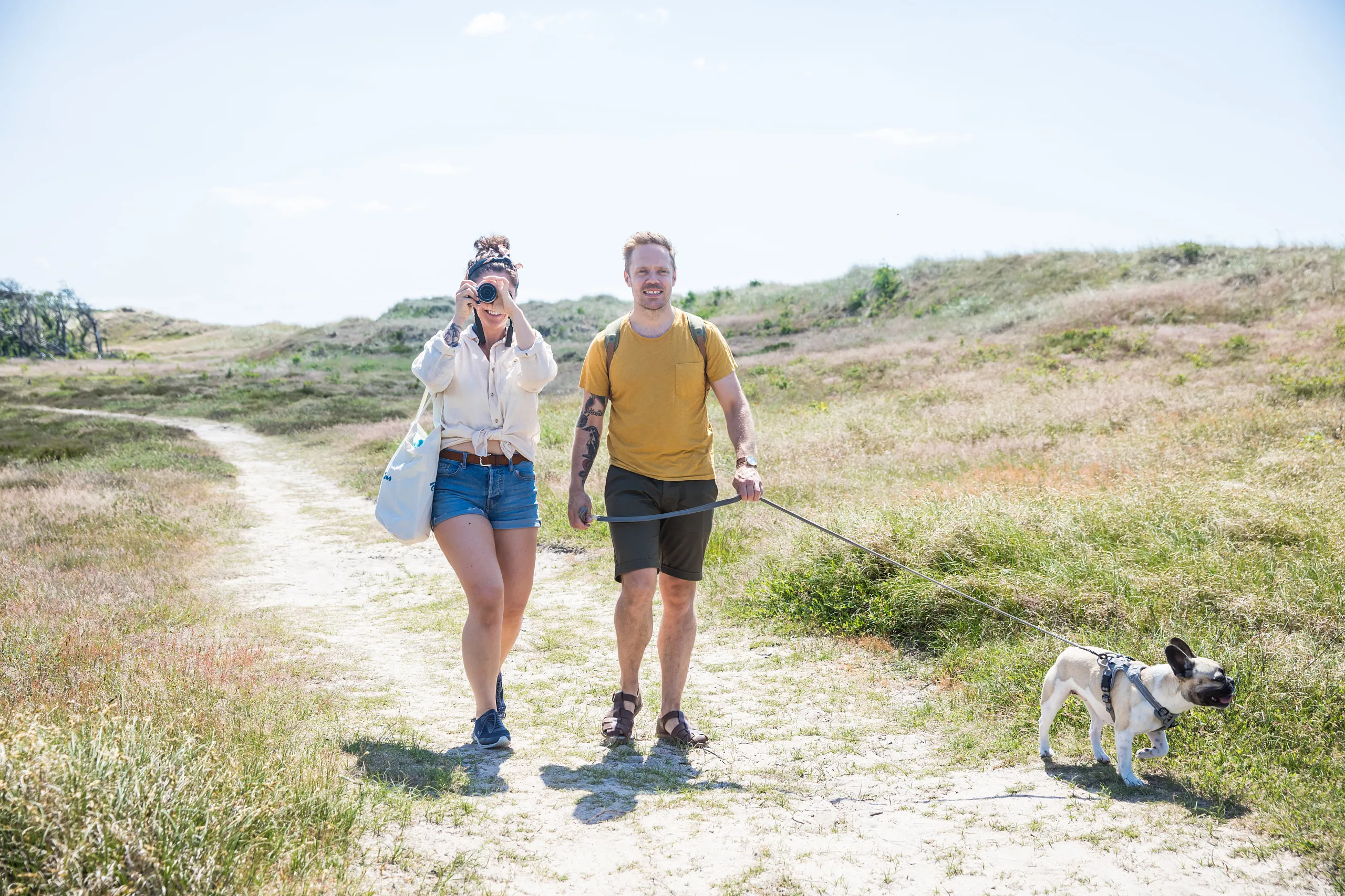 Par med hund som promenerar över strandäng.