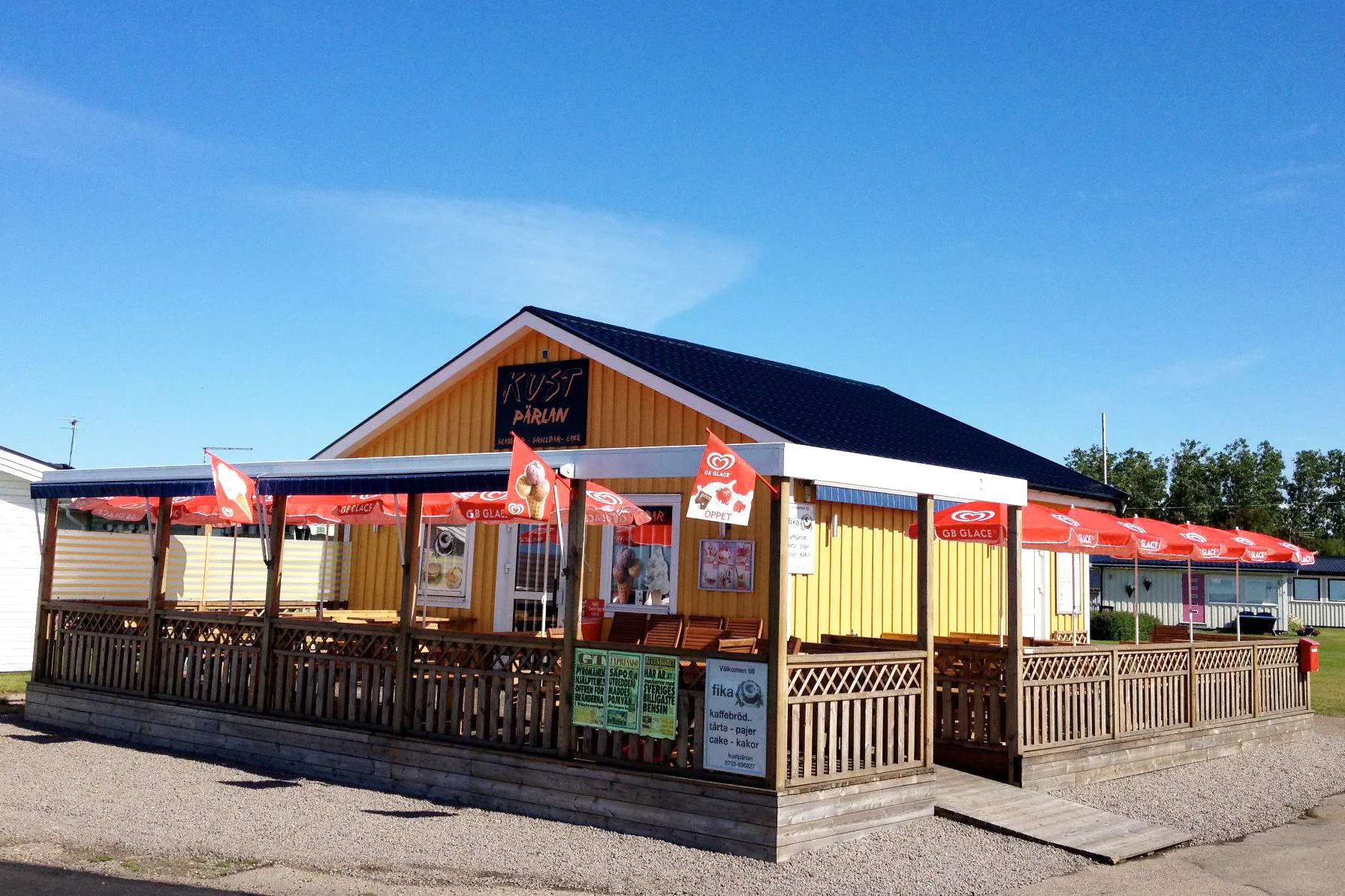 Gul glasskiosk med röda parasoller på uteserveringen.