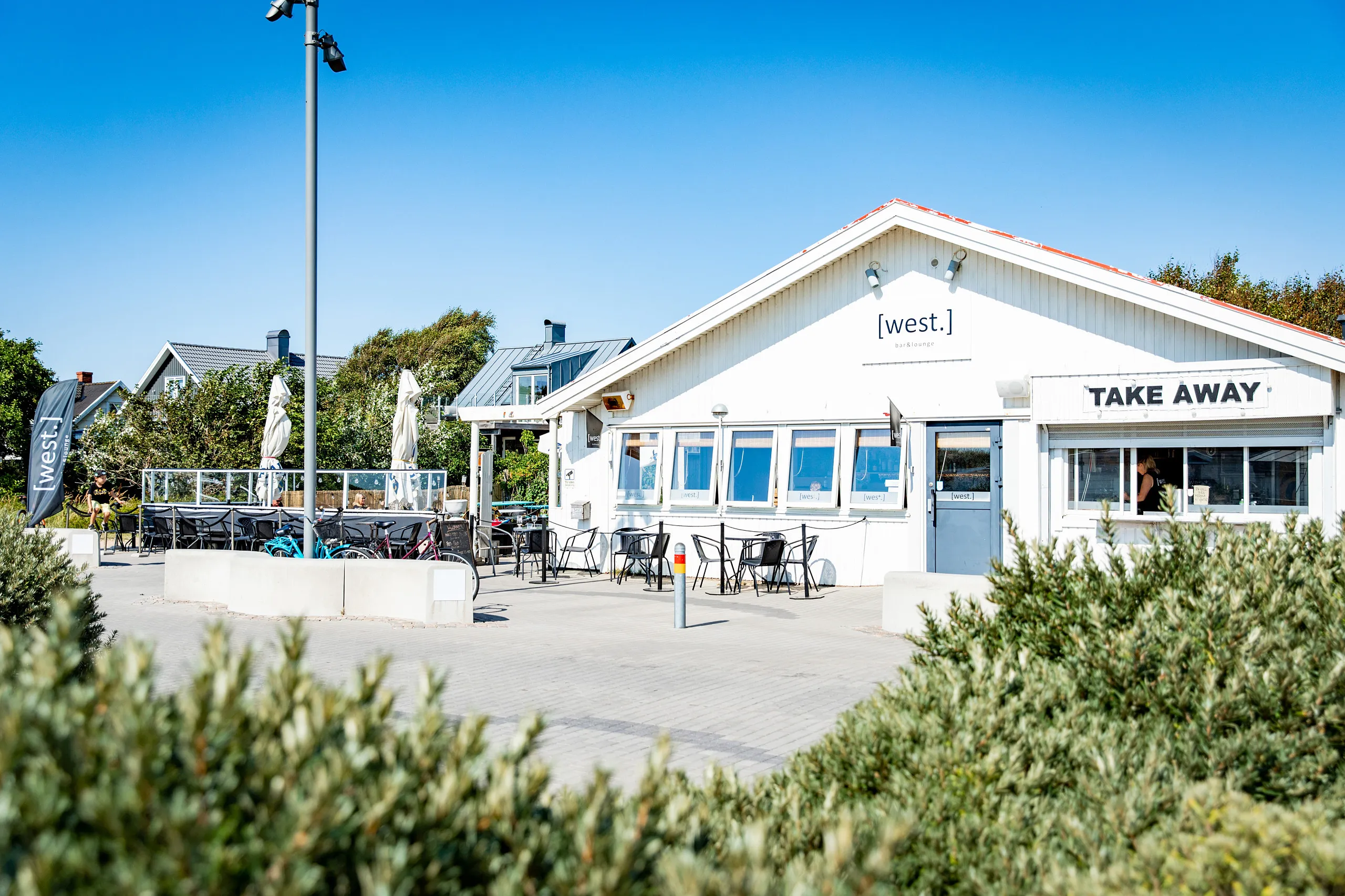 Vit fasad på restaurangen med växtlighet i förgrunden..