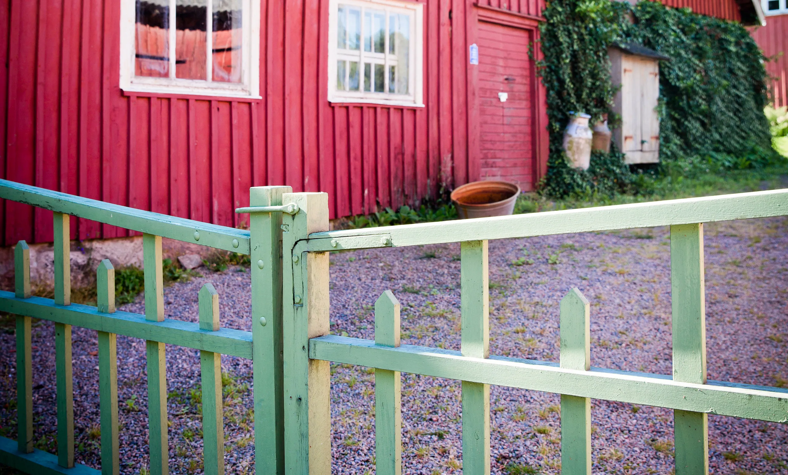 Närbild på en grön grind framför ett rött hus