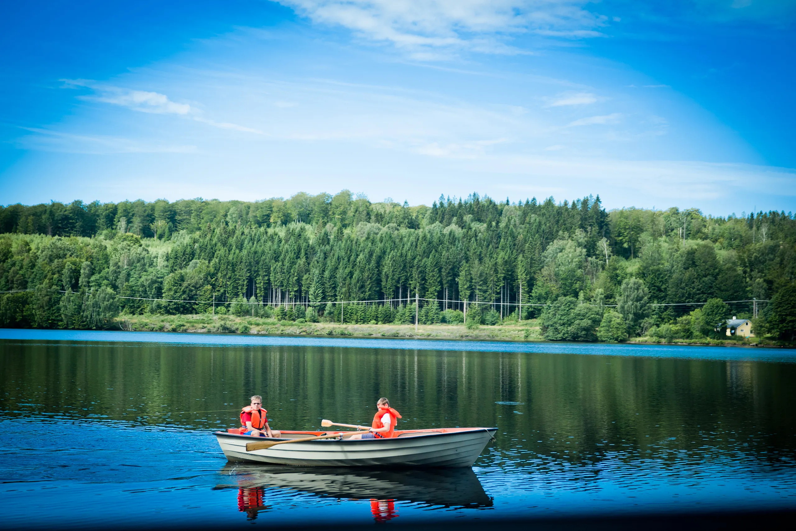 Två barn sitter i en eka på en sjö omgiven av skog