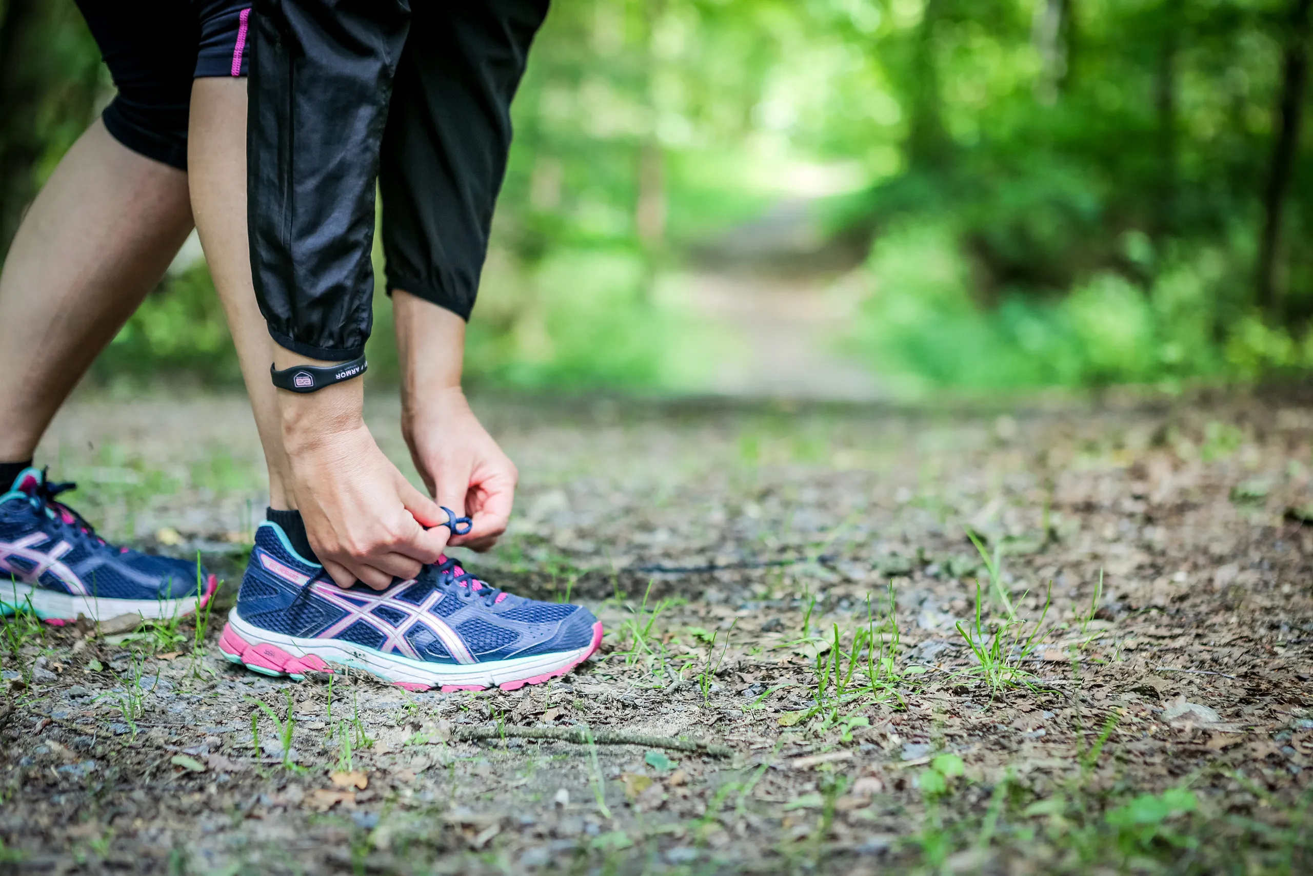 Närbild på en person som knyter på sig löparskor på en grusväg
