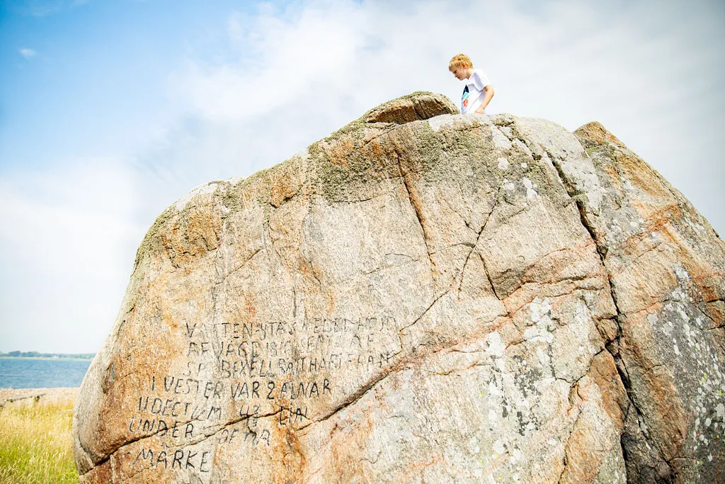 Ett barn står på en stor sten med inristade ord