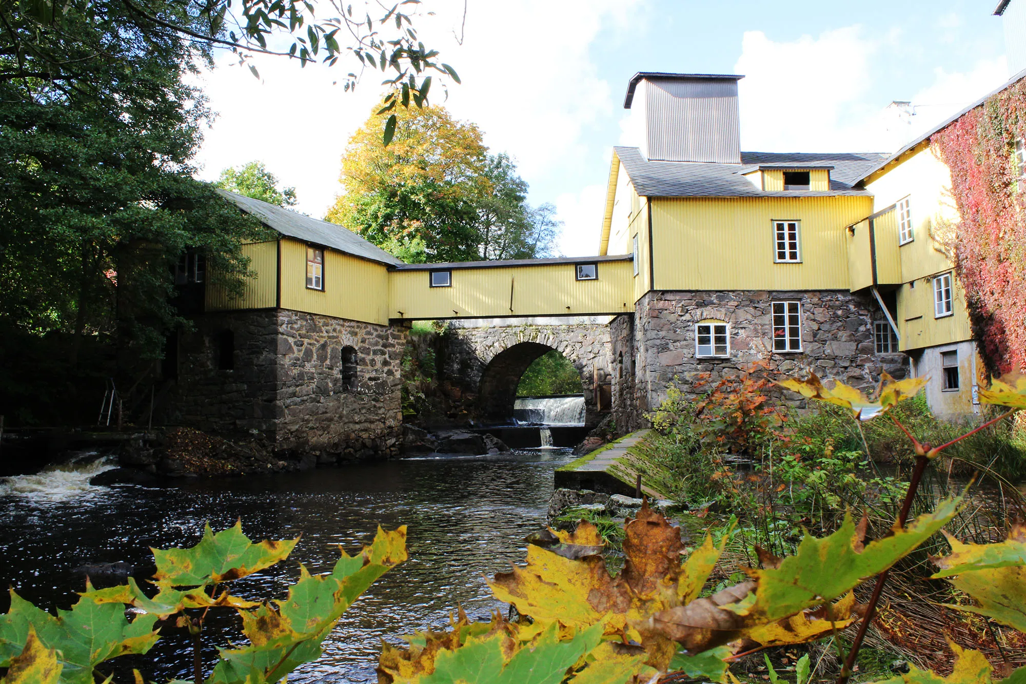 En gul kvarnbyggnad över vattendrag.