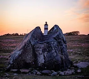 fyr bakom sten i fält av trift i solnedgång