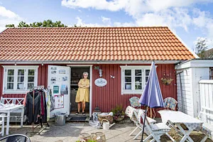 Kvinna står i dörröppningen till ett rött hus och inredningsbutik.