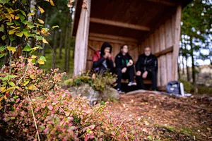 tre personer fikar i vindskydd i skog
