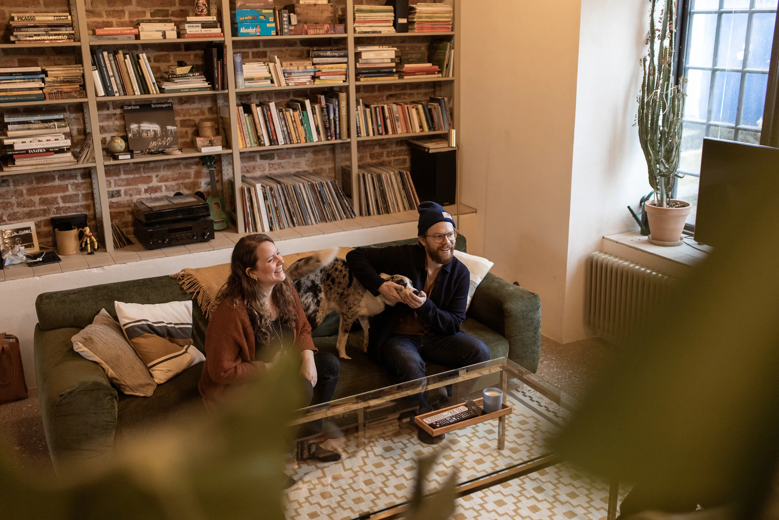 Två personer sitter i en soffa med en hund