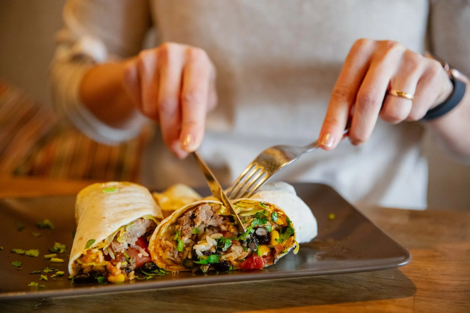 En burrito på tallrik med två händer som håller bestik och delar den.