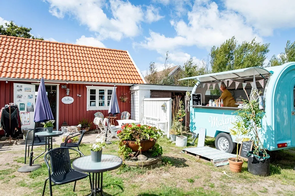 En liten röd stuga med en turkos foodtruck bredvid.