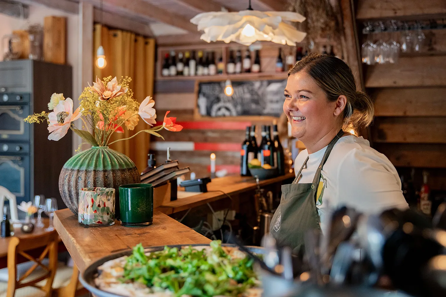 En kvinna står bakom en bardisk i restaurangmiljö.