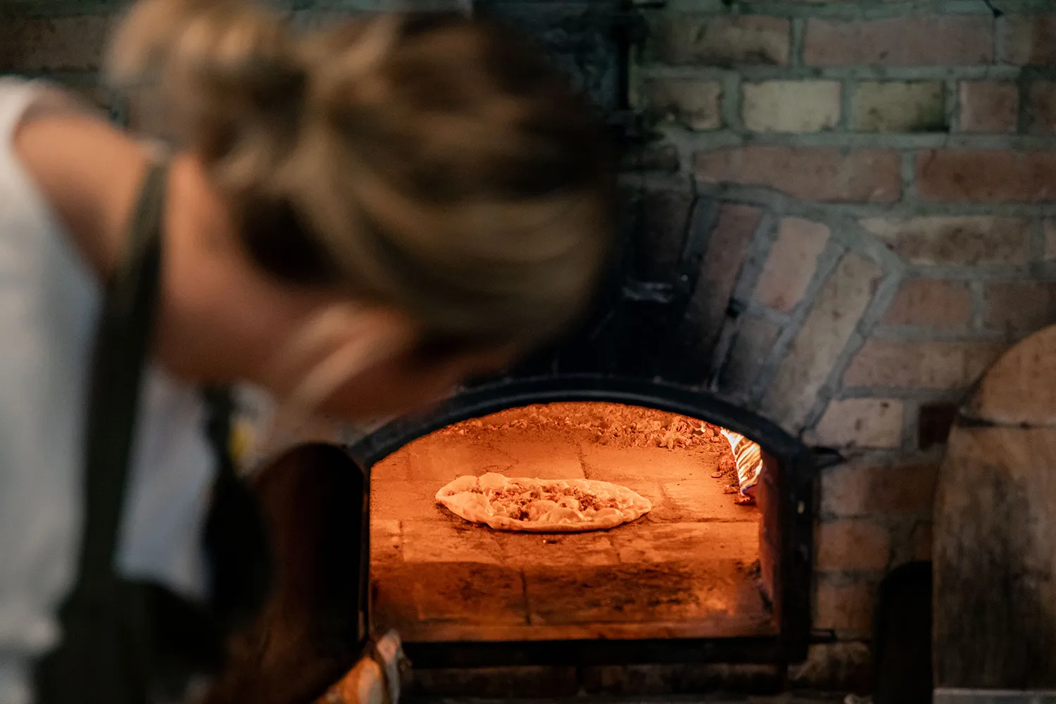 En person tittar in i i pizzaugn där en pizza gräddas.