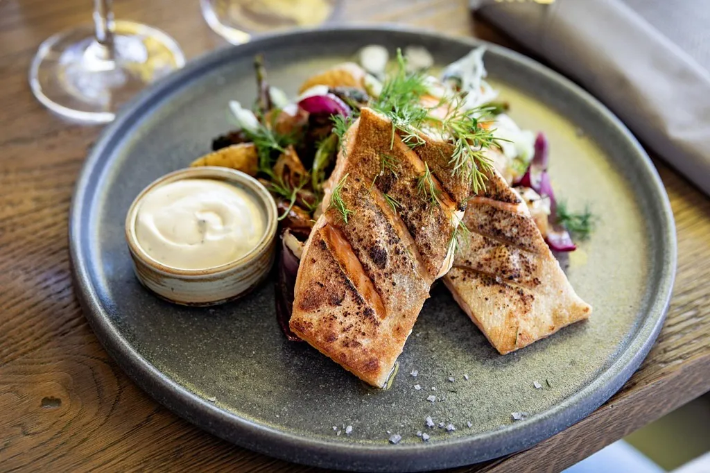 En tallrik med fjällrödning, potatis och sås i en liten skål.