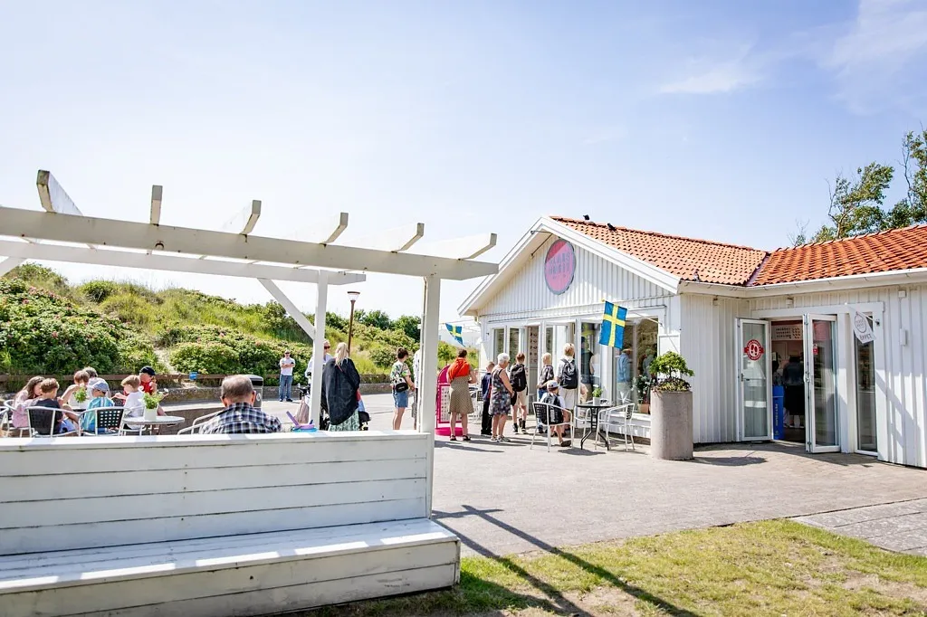 Glasshuset, vit byggnad med uteservering och sanddynor i bakgrunden.