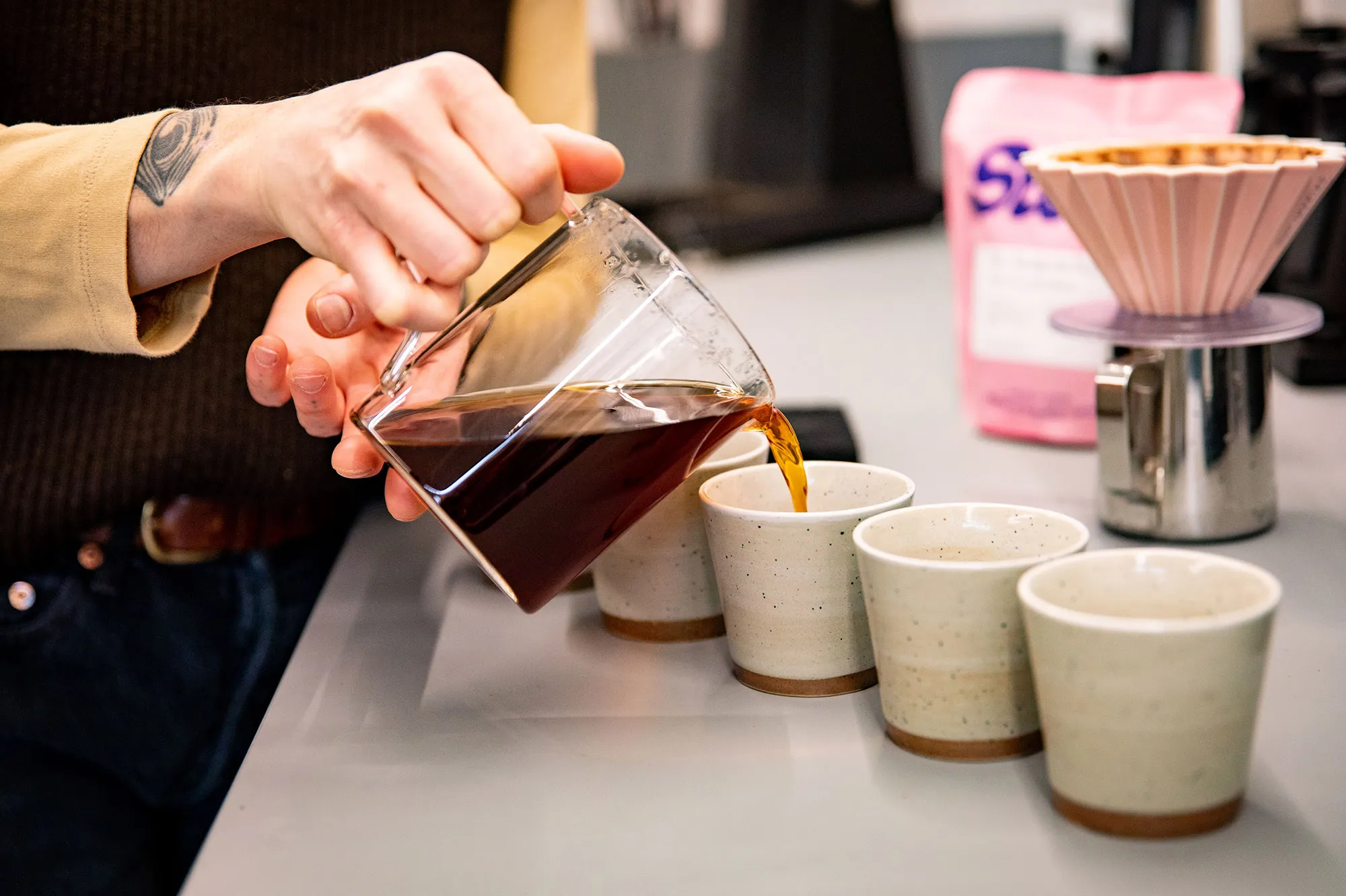 Närbild på hand som häller upp kaffe i fyra koppar.