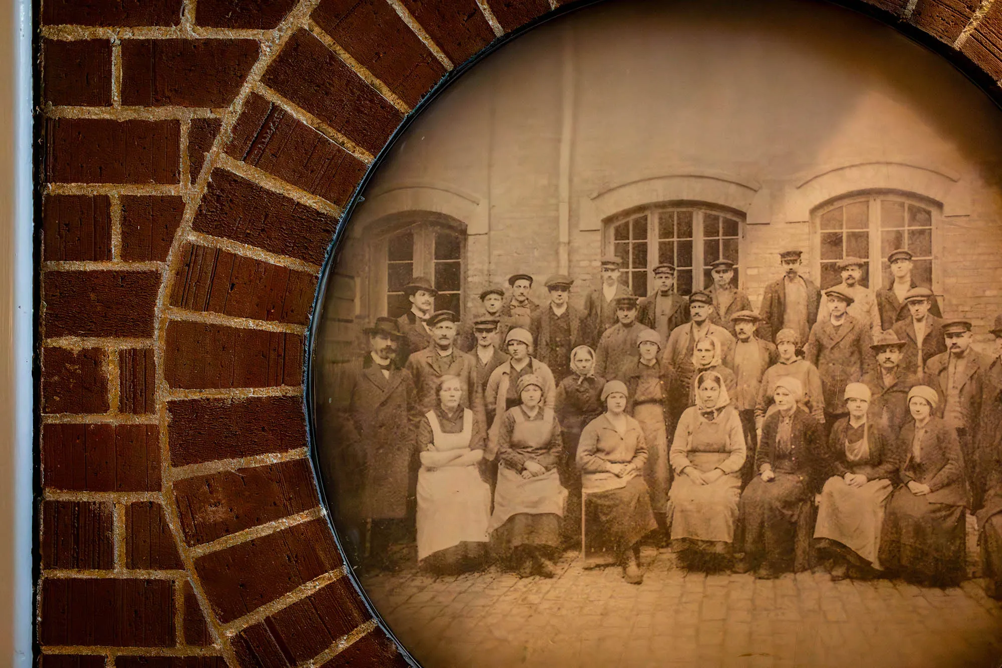 Tegelvägg med ett inmurat gammalt svartvitt fotografi med en samling människor.