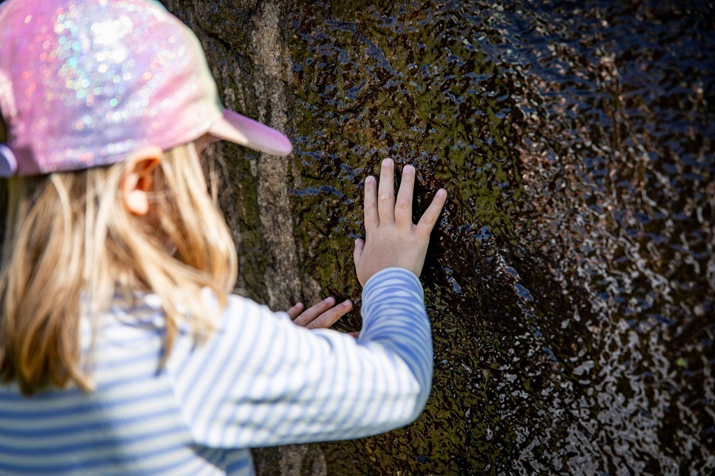 En flicka känner på ett stenkonstverk med rinnande vatten