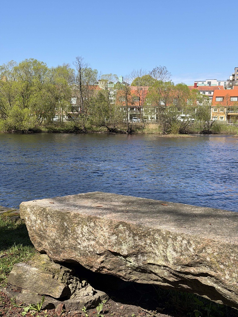 en stenbänk vid vatten med grönska i bakgrunden